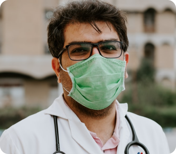 A doctor wearing a surgical mask and stethoscope outside a hospital.